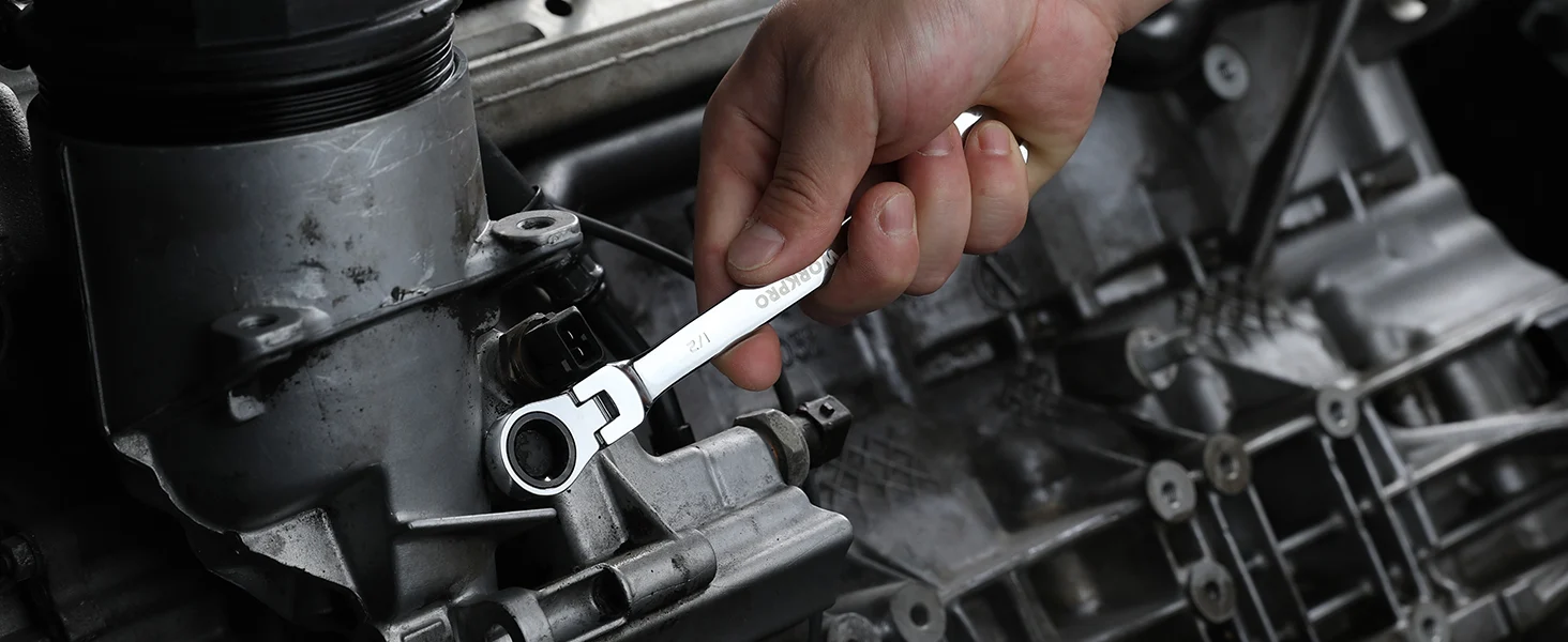 Hand holding a wrench on a car engine, with metal parts and hoses in a close mechanical workspace