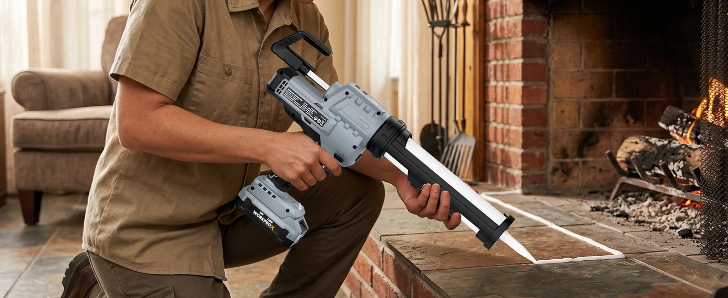 Person holding a gray cordless power tool with a long blade, standing near a brick fireplace and tools