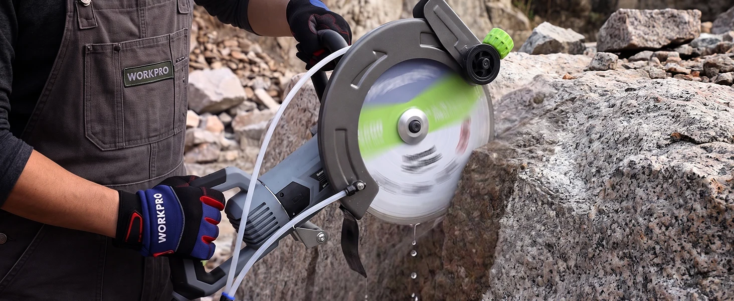 Handheld circular saw cutting stone outdoors, with green wheel guard and protective gloves on rocky ground