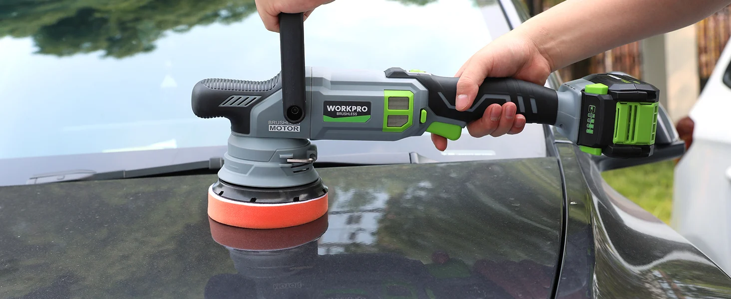 Hand holds a cordless power sander with a green battery, polishing a dark metal surface outdoors