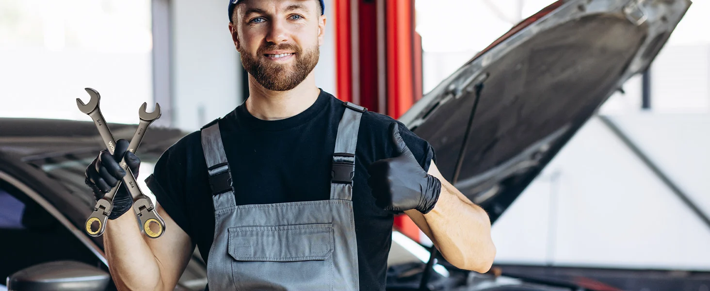 Mechanic in gray overalls with wrenches and a raised car hood, innovation and quality in workshop repair