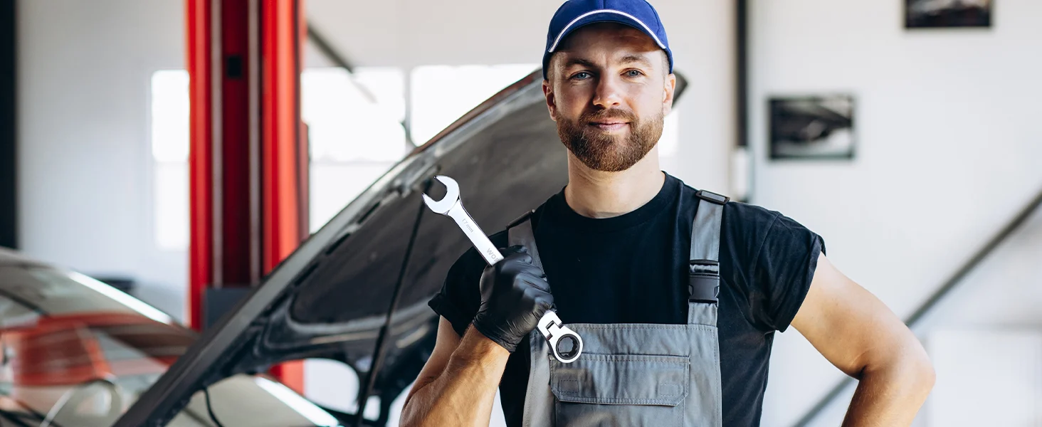 Automotive worker in a blue cap and gray apron holding a wrench, with innovation and quality in a garage setting
