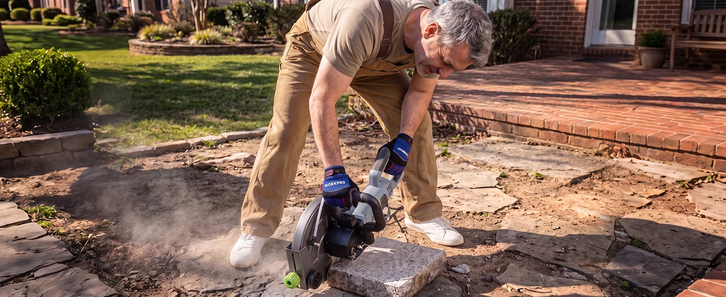Man using a power saw to cut stone pavers on a brick patio, dust rising in daylight