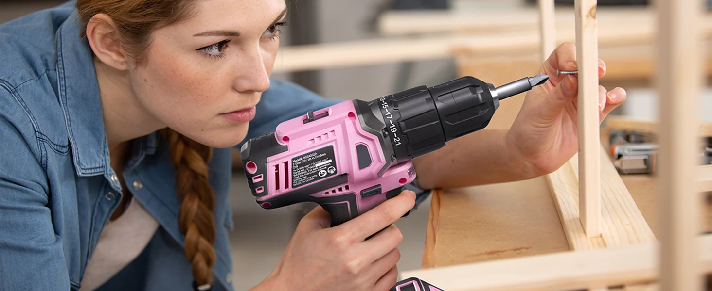 Woman uses a pink and black power drill to screw a wooden board in a workshop, showing innovation and quality