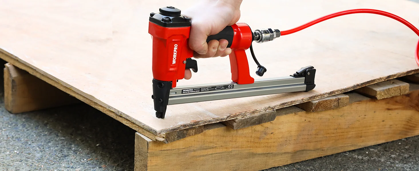 Hand holding a red stapler gun on wooden boards, showing innovation and durable fastening quality