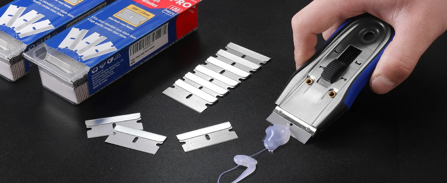 Hand holding a metal blade tool with multiple razor blades and blue packaging on a dark surface