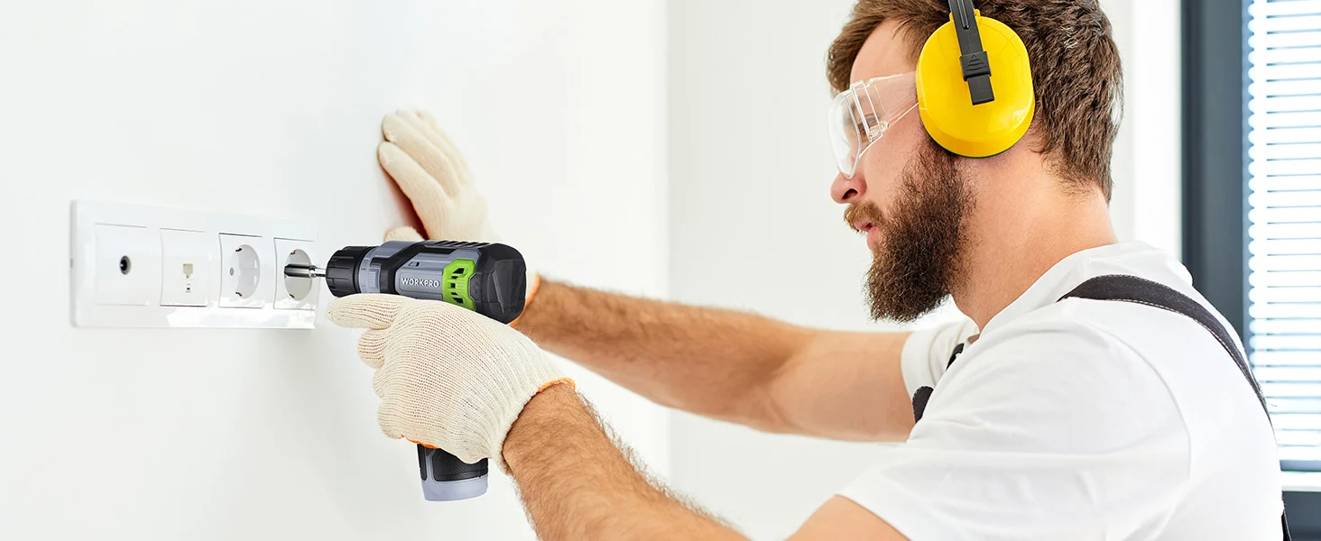 Electric drill in use by a worker with protective earmuffs and gloves, installing a wall outlet for secure quality